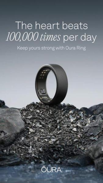 A minimalist studio shot of an Oura Ring perched on a bed of dark, raw charcoal-like stone against a soft, neutral gradient background.